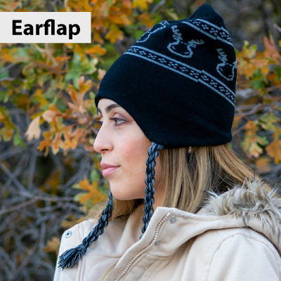 Woman wearing a black knit beanie with earflaps against a natural background